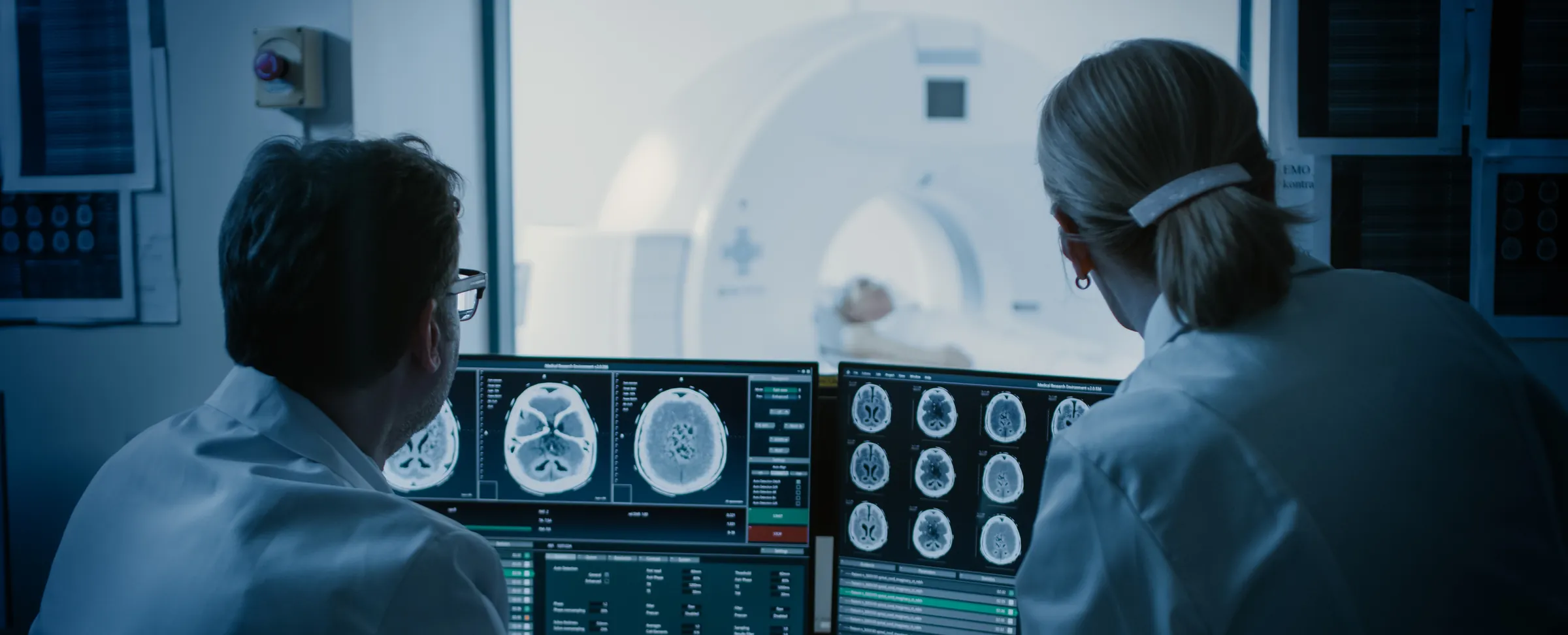 Two medical radiation technologists reviewing CT brain scans on monitors beside a scanner suite